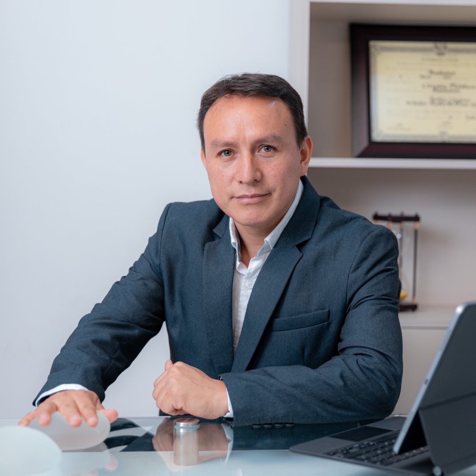 Dr. Wilder Díaz en consultorio, junto a su diploma y un implante mamario